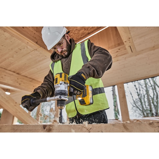 Side shot of construction worker using 18V XR Brushless Premium Hammer Drill Driver with 8Ah battery to drill a hole in wood