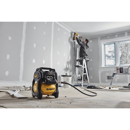 A TRADESMAN USING A DCC1018 COMPRESSOR WITH A NAILER TO INSTALL CORNICE