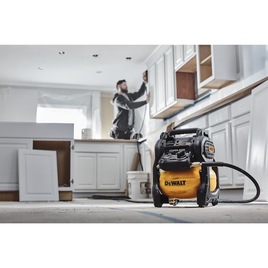 A TRADESMAN USING A DCC1018 COMPRESSOR WITH A NAILER TO INSTALL TRIM TO A KITCHEN CABINET