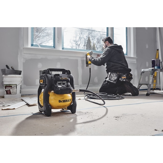 A TRADESMAN USING A DCC1018 COMPRESSOR WITH A NAILER TO INSTALL PANELING