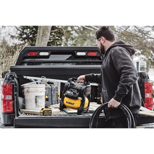 A TRADESMAN TAKING A DCC1018 CORDLESS AIR COMPRESSOR FROM THE BACK OF A TRUCK