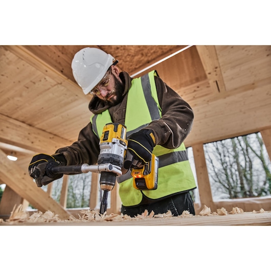 Side shot of construction worker using 18V XR Brushless Premium Hammer Drill Driver with 5Ah Powerstack to drill a hole in wood