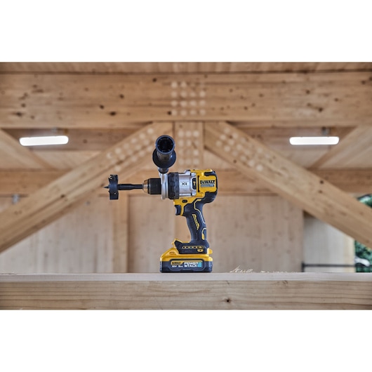 Side view of 18V XR Brushless Premium Hammer Drill Driver with side handle and Powerstack 5Ah battery sitting on top of a wooden table