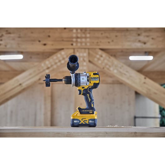 Side view of 18V XR Brushless Premium Hammer Drill Driver with side handle and 8Ah battery sitting on top of a wooden table