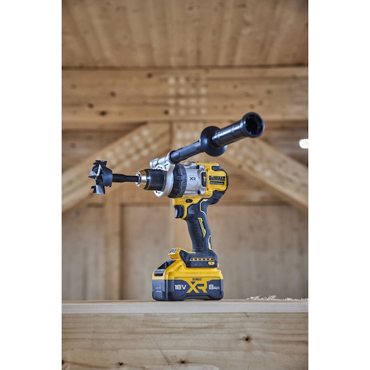 Angled view of 18V XR Brushless Premium Hammer Drill Driver with side handle and 8Ah battery sitting on top of a wooden table