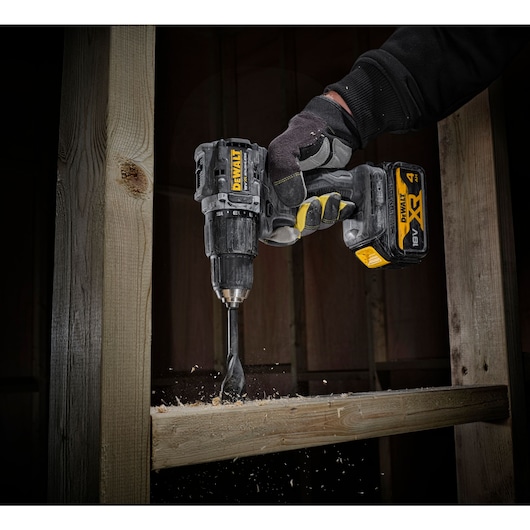 close up view of the DCD100 drilling through timber stud wall using one hand