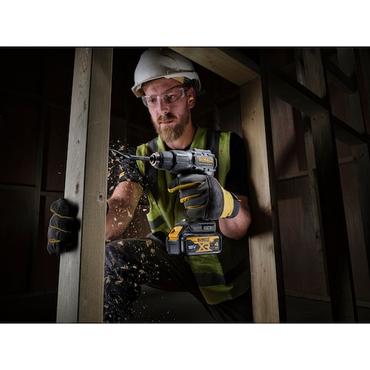Worker in high vis drilling through timber stud wall