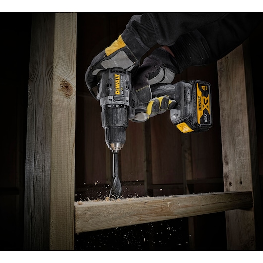 close up view of the DCD100 drilling through timber stud wall using both hands