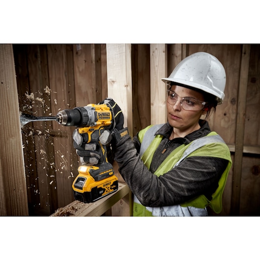 A PERSON USING A DEWALT DCD800 18V XR DRILL DRIVER WITH A 5AH BATTERY DRILLING THROUGH TIMBER STUD WALL