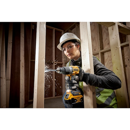 A PERSON USING A DEWALT DCD805 18V XR HAMMER DRILL DRIVER WITH A COMPACT POWERSTACK BATTERY DRILLING THROUGH TIMBER STUD WALL