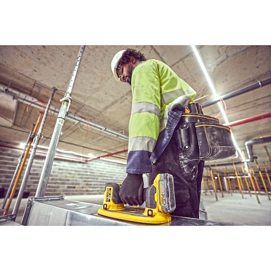 Construction worker preparing to use the Grabo 18V XR Suction Lifter to carry metal duct framework, wearing tool belt