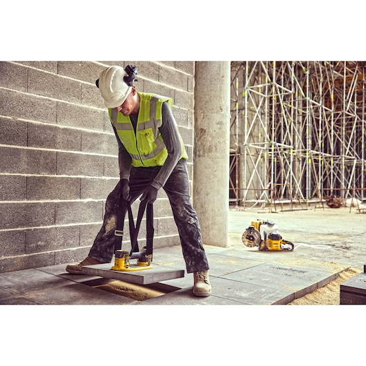 Construction worker uses the straps of a Grabo 18V XR Suction Lifter to lower a concrete block into position