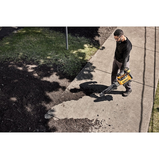 Viewed from above, a worker uses 54V Axial Blower DCMBL777 to clear bark away from a pavement