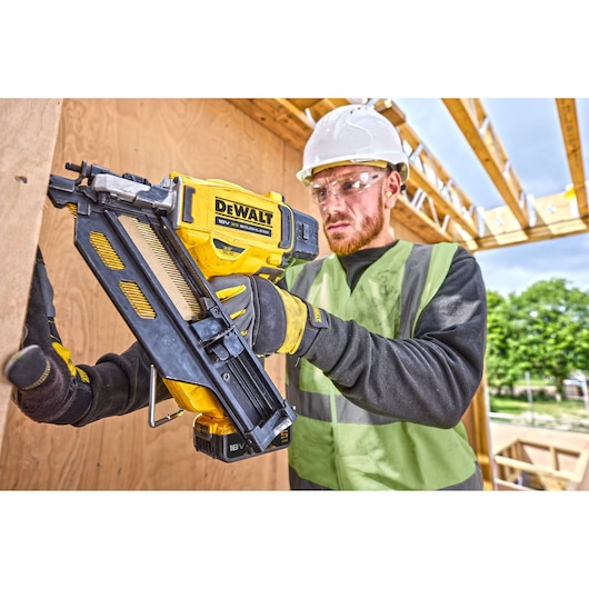 Worker using DCN930 18V XR Brushless framing nailer to drive nails into a wooden frame