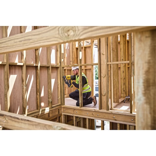 Worker using DCN930 18V XR Brushless framing nailer on  the internal wooden frame of a building construction