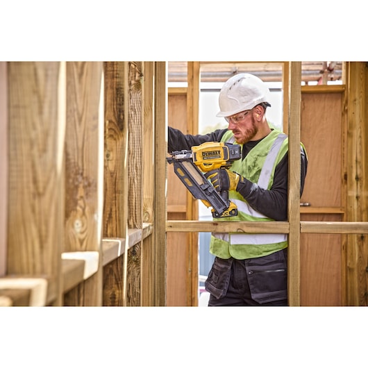 Wooden framing surrounds a construction worker using DCN930 18V XR Brushless framing nailer