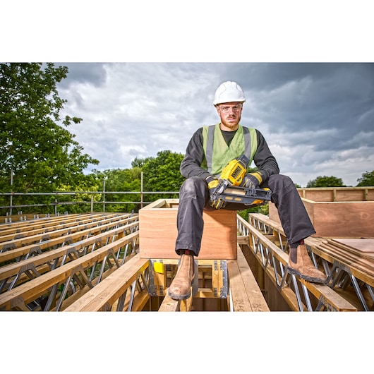 Construction worker sitting on top of a rooftop holding a DCN930 18V XR Brushless framing nailer