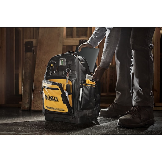 Person adding a laptop into the Dewalt Pro backpack, on a construction site